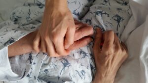 Holding hands with an elderly loved one during end-of-life care, symbolizing patient-centered geriatric support