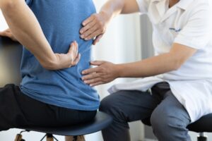 Male patient receiving a back pain evaluation during a clinical consultation with a doctor