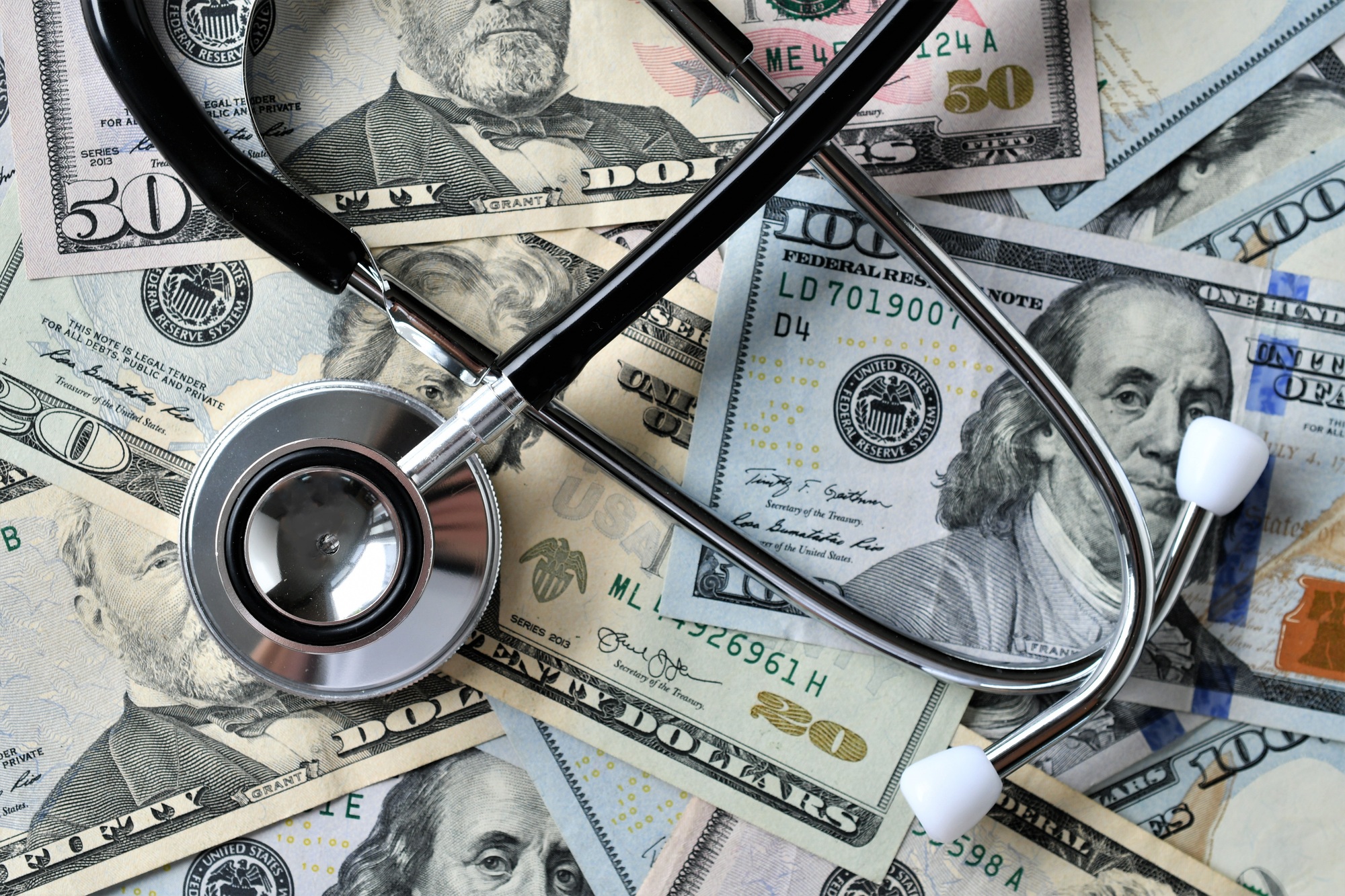 Stethoscope resting on stacks of dollar bills, symbolizing the influence of money in modern healthcare.