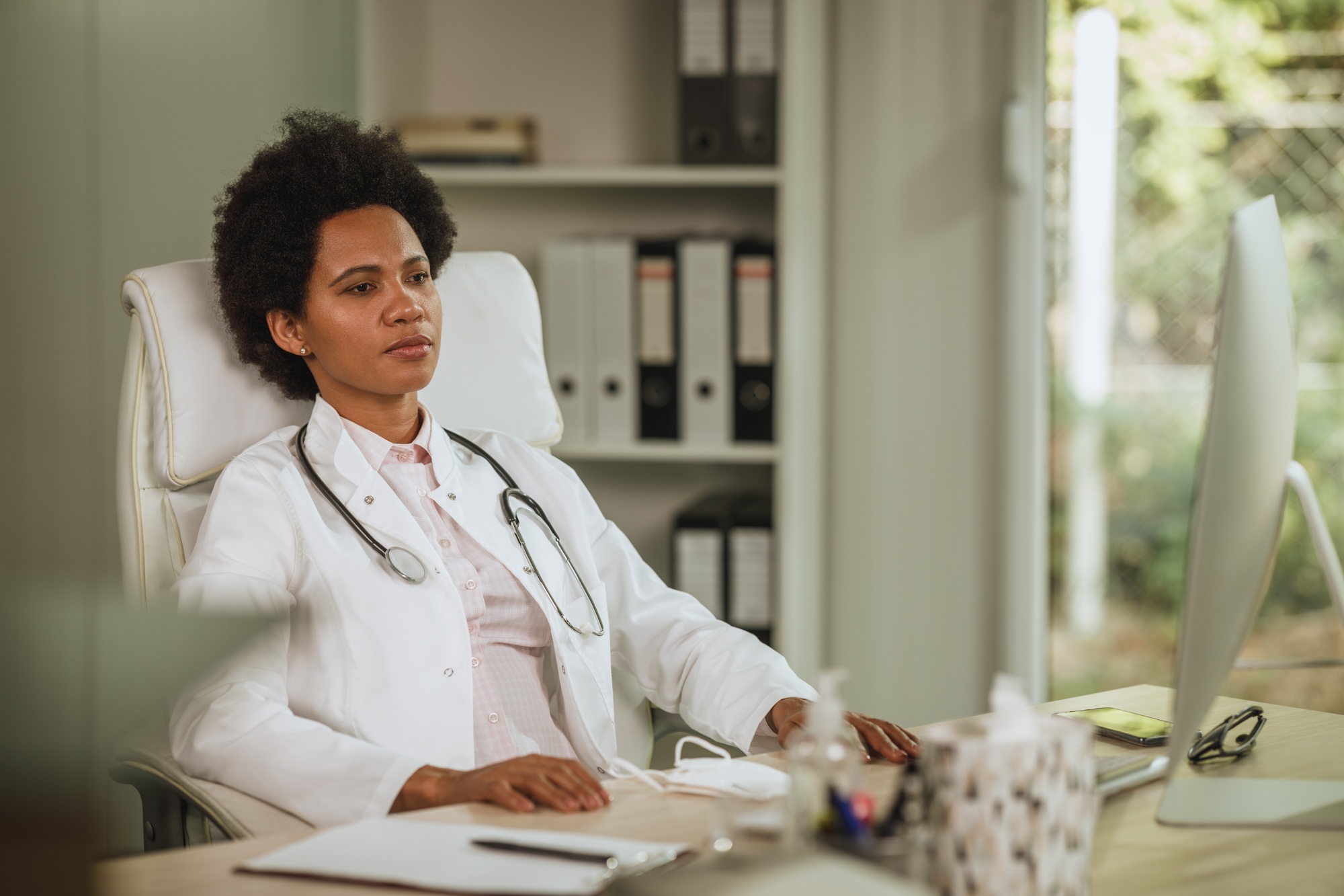 A fatigued female doctor sits at her desk, staring blankly—symbolizing healthcare burnout and the pressures facing today’s medical professionals.