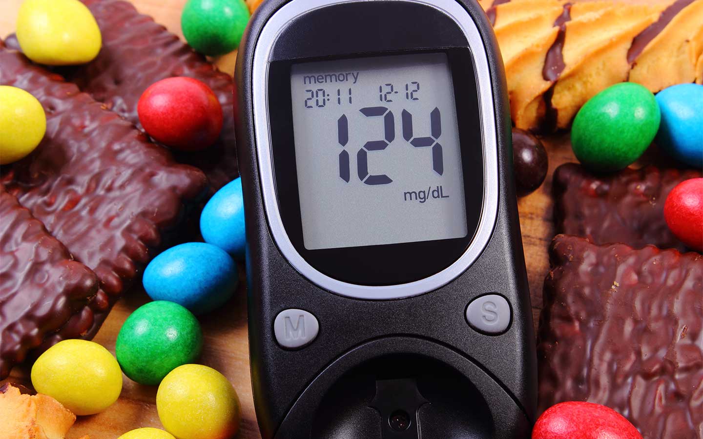 Glucometer beside a heap of candies and cookies, illustrating a prediabetes diagnosis and reducing sugary foods