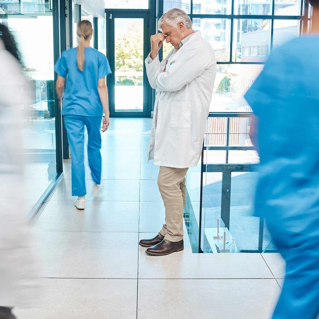 Overwhelmed doctor in a hospital corridor, illustrating the primary care crisis and clinician burnout