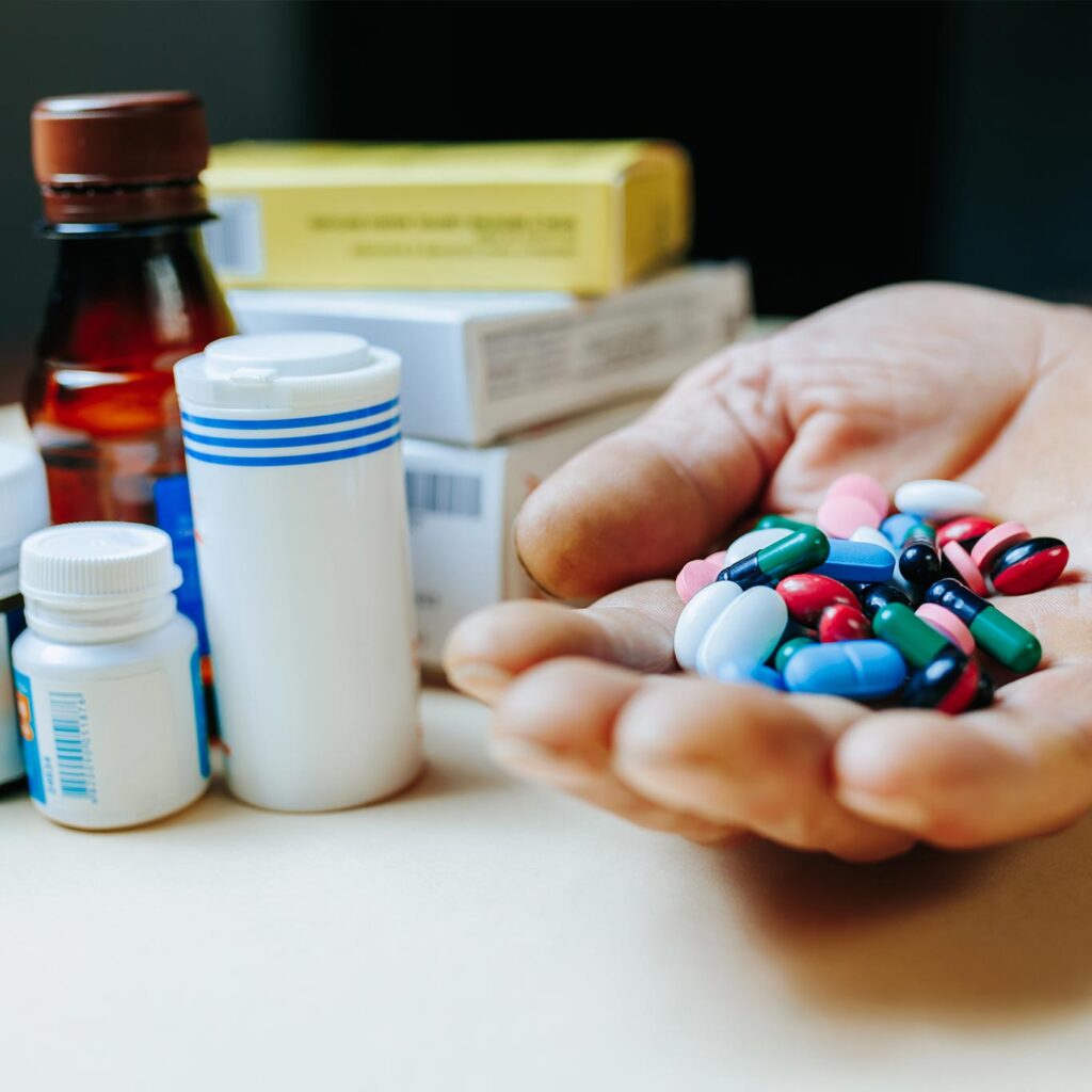Hand holding multiple pills beside prescription bottles, illustrating the escalator from Zetia to PCSK9 inhibitors like Repatha under new cholesterol guidelines
