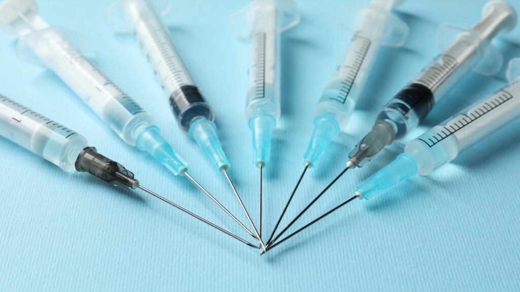Multiple syringes arranged on a blue background, illustrating getting multiple vaccines at once and vaccine stacking
